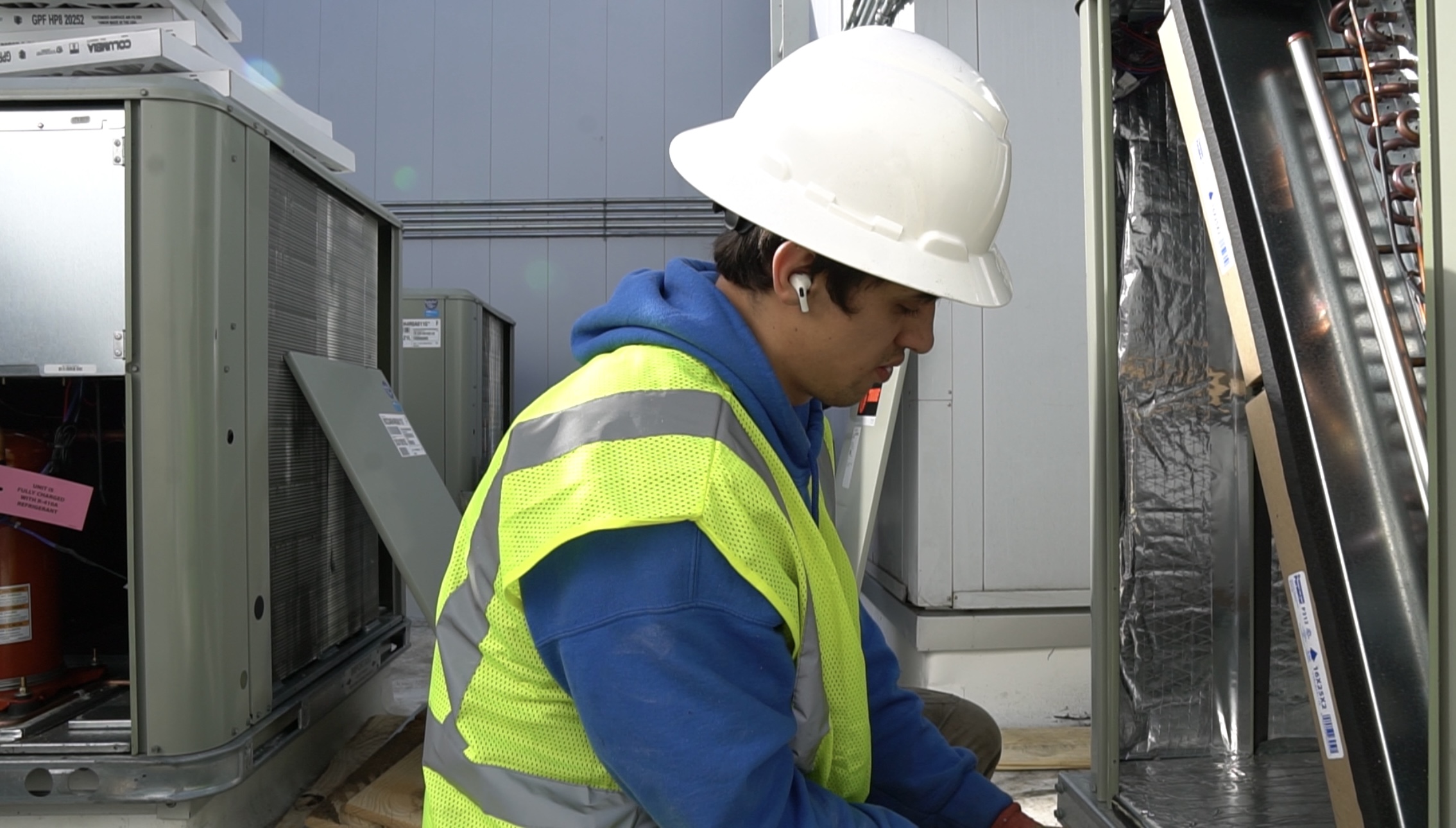 HVAC technician in hard hat inspects the internal components of a rooftop unit while preparing for system installation.