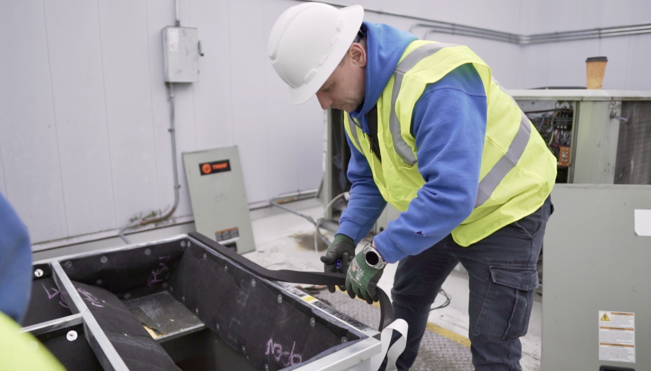 Worker applies weatherproof sealing tape around the base frame of a rooftop HVAC unit during system preparation and installation.