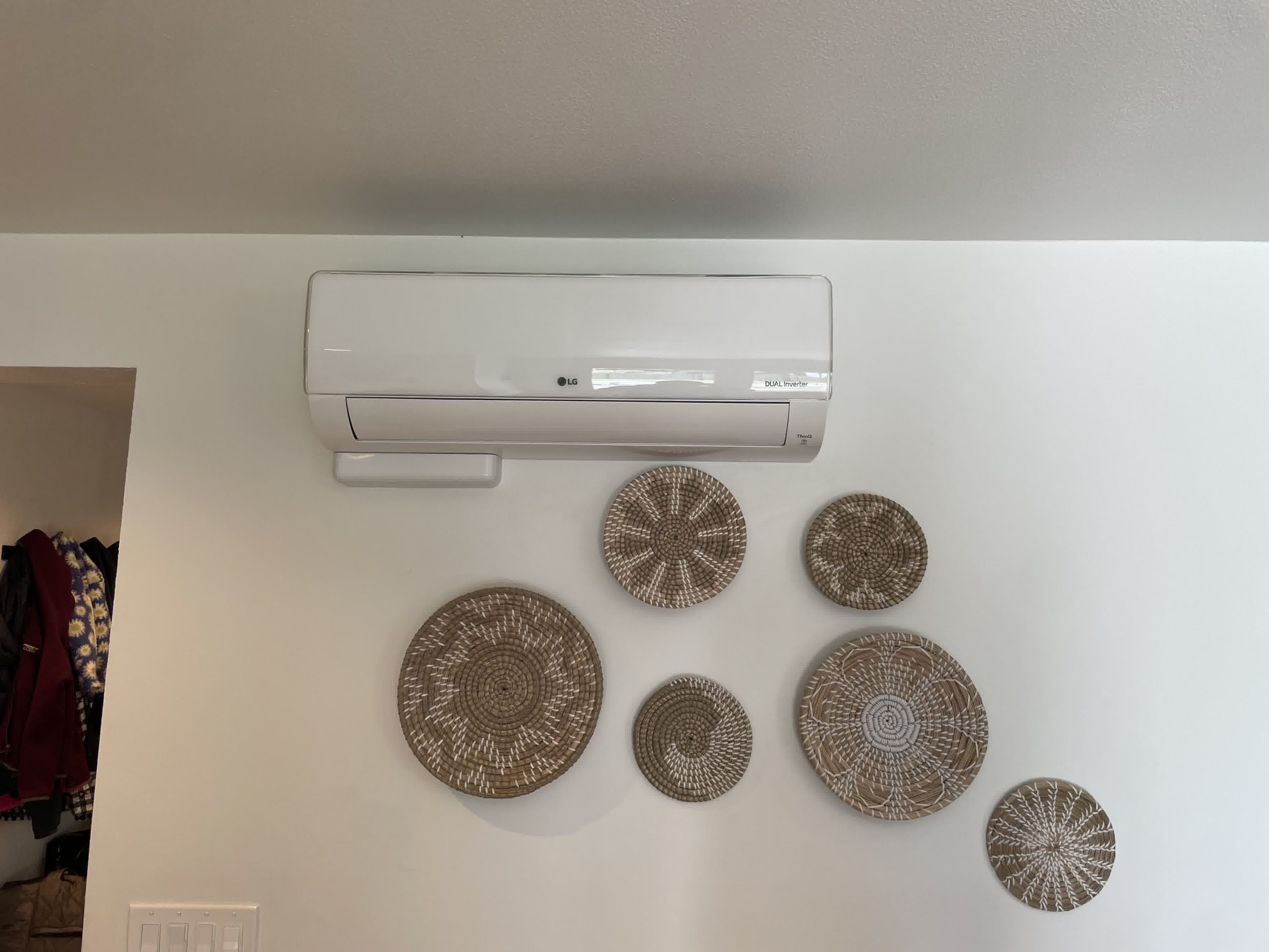 LG mini split AC unit mounted above decorative woven baskets on a white wall inside a modern, minimally decorated home.