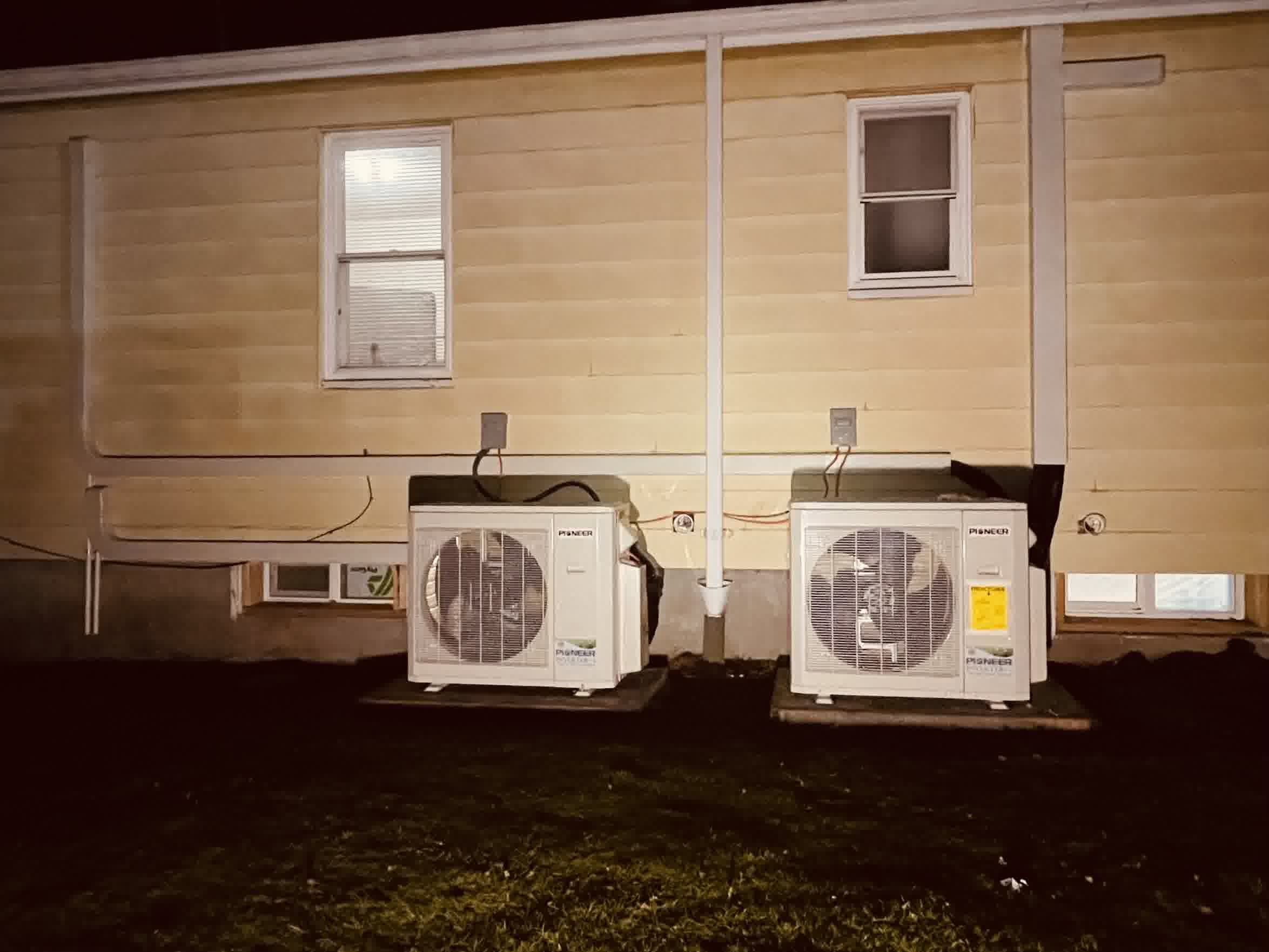 seattle sod installation irrigation kirkland lawn setup sprinkler install - Seattle Heating & Cooling Two outdoor Pioneer mini split condenser units sit on concrete pads against a yellow house with visible wiring and windows at night.