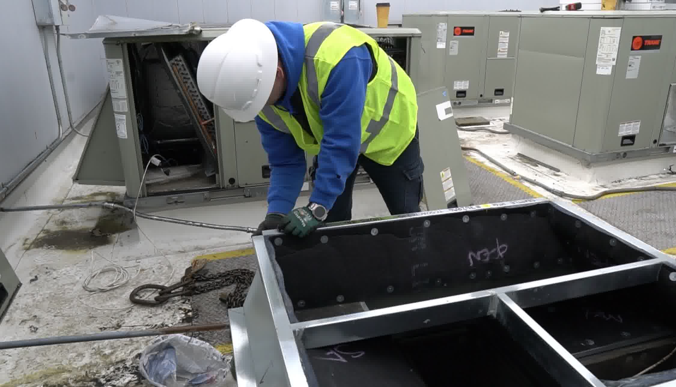 HVAC technician in safety gear installing rooftop AC unit, securing components for efficient cooling system performance.