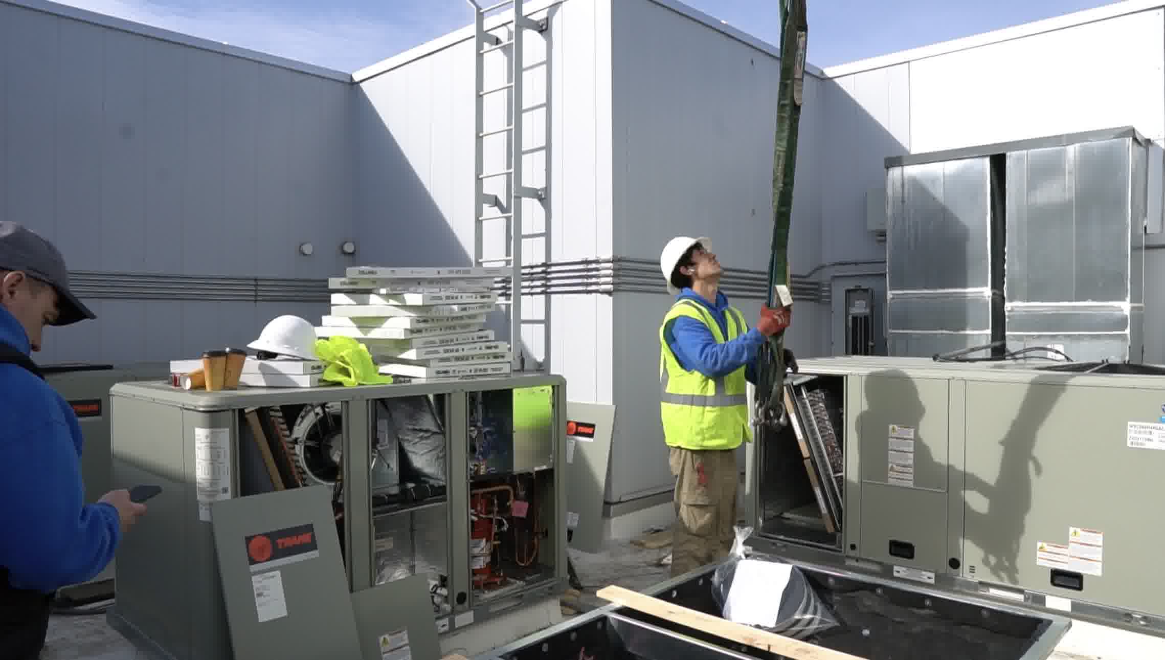 Team preparing rooftop AC installation, lifting unit parts with crane for precise placement and secure setup.